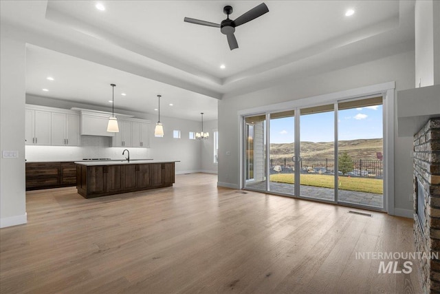 kitchen with dark brown cabinetry, a mountain view, an island with sink, white cabinets, and ceiling fan with notable chandelier