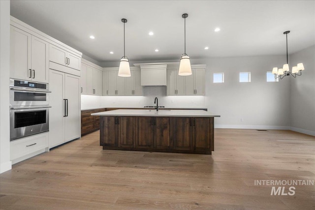 kitchen featuring a kitchen island with sink, pendant lighting, and stainless steel double oven