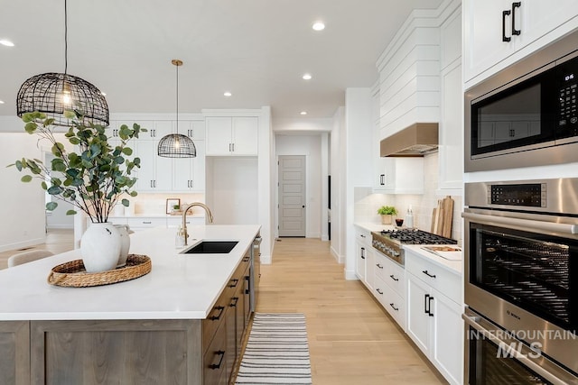 kitchen with decorative light fixtures, sink, stainless steel appliances, and an island with sink