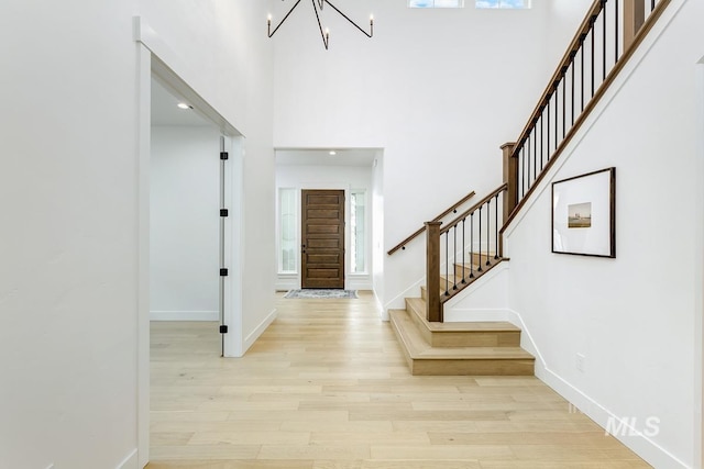 foyer entrance with light wood-type flooring, a notable chandelier, and a towering ceiling