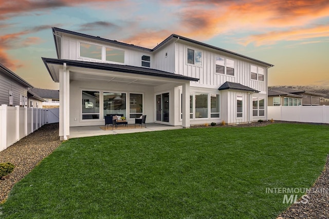 back house at dusk featuring a lawn and a patio area