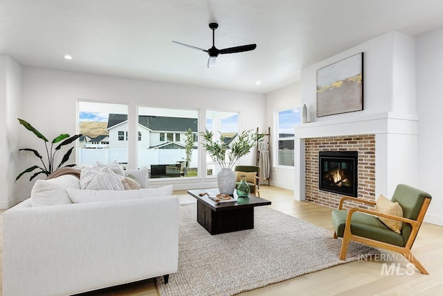 living room featuring ceiling fan, a brick fireplace, and hardwood / wood-style floors