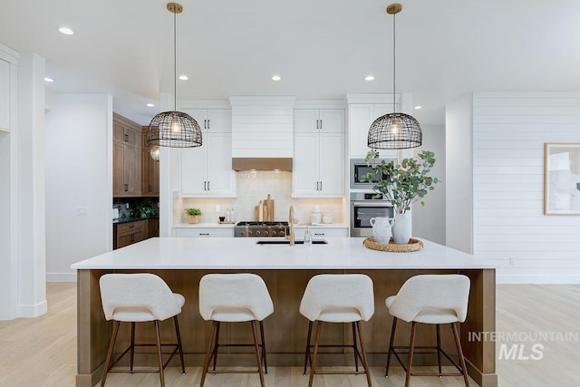 kitchen featuring a kitchen island with sink, hanging light fixtures, oven, wall chimney exhaust hood, and sink