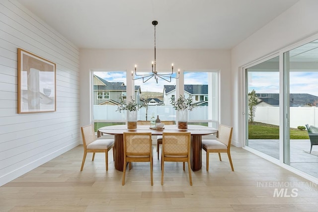 dining area featuring wood walls, light hardwood / wood-style flooring, and a notable chandelier