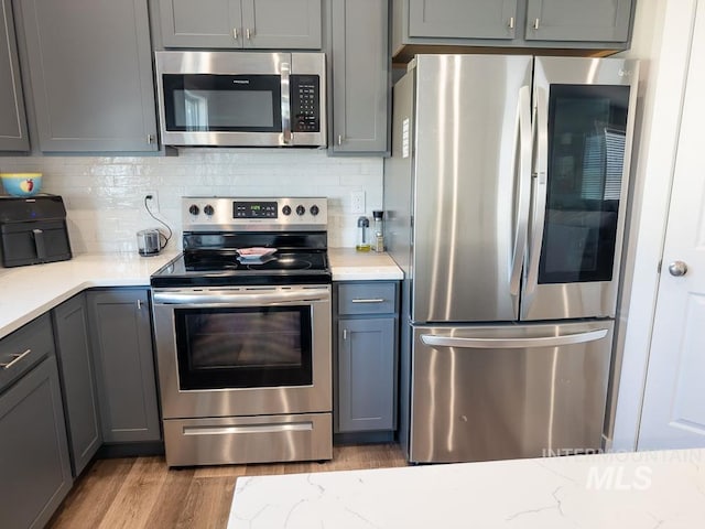 13743 S Sonata Way, Nampa, ID 83651 - kitchen featuring stainless steel appliances, gray cabinets, wood finished floors, decorative backsplash, and light stone counters
