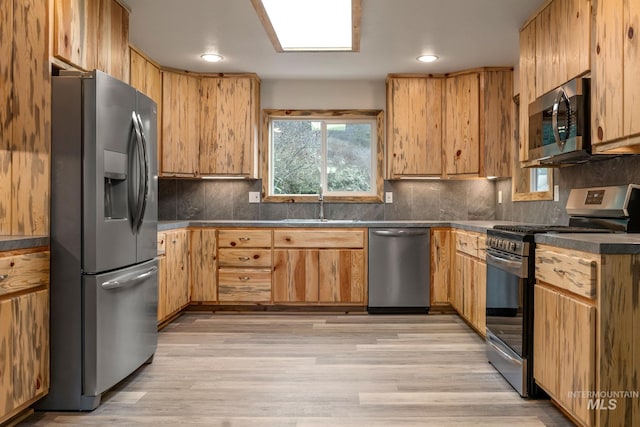 kitchen with decorative backsplash, appliances with stainless steel finishes, light wood-type flooring, and sink