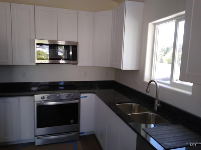 kitchen with stainless steel appliances, white cabinetry, dark stone countertops, and sink