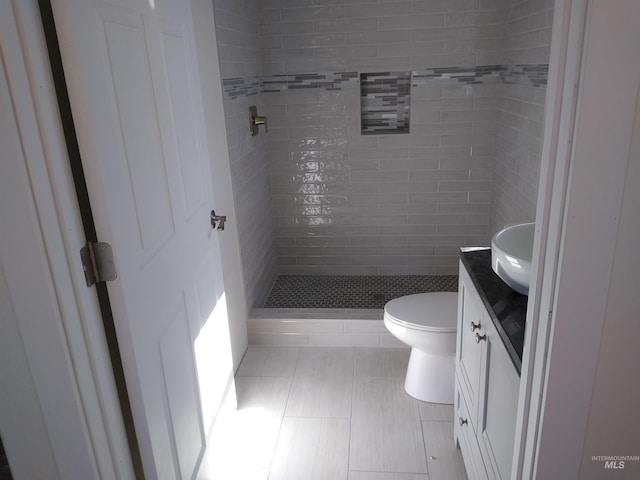 bathroom featuring a tile shower, tile patterned floors, vanity, and toilet