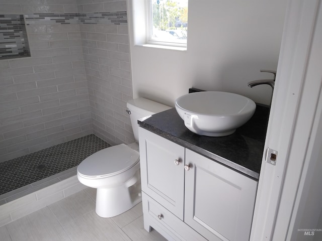 bathroom with tiled shower, tile patterned floors, vanity, and toilet