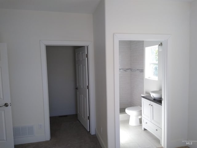 bathroom with tiled shower, tile patterned flooring, vanity, and toilet