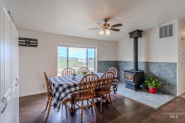 3537 Brogan Rd, Emmett, ID 83617 - dining area featuring a wood stove, wood finished floors, a ceiling fan, and a wainscoted wall
