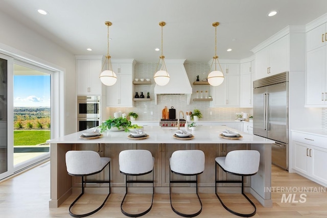 kitchen with a large island, appliances with stainless steel finishes, custom range hood, and white cabinetry