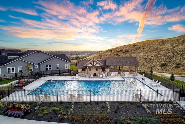 pool at dusk featuring a mountain view and a patio