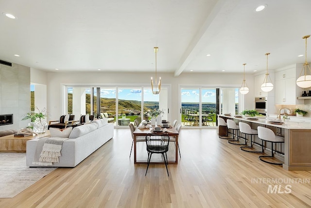 living room with light hardwood / wood-style floors, beam ceiling, a tiled fireplace, and a notable chandelier