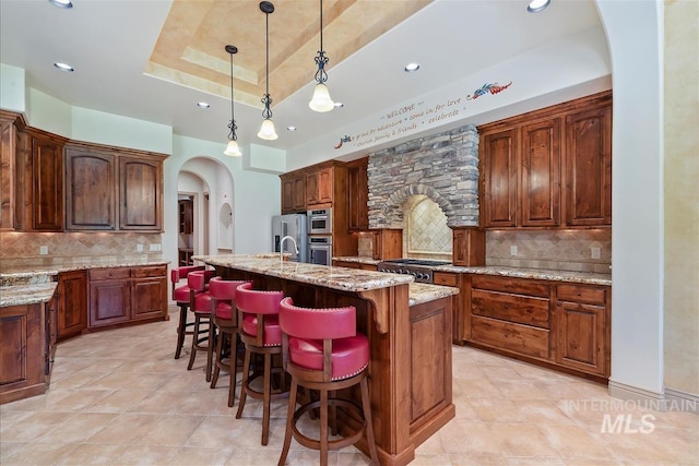 215 W Riverbridge Ln, Eagle, ID 83616 - kitchen with appliances with stainless steel finishes, arched walkways, decorative backsplash, a kitchen island with sink, and light stone counters