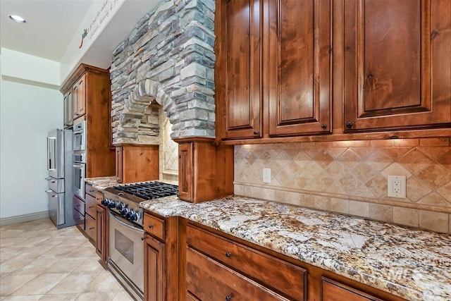 215 W Riverbridge Ln, Eagle, ID 83616 - kitchen featuring stainless steel appliances, backsplash, light stone countertops, brown cabinets, and light tile patterned floors