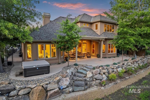 215 W Riverbridge Ln, Eagle, ID 83616 - back of property at dusk featuring a hot tub, a patio, a chimney, a gate, and stucco siding