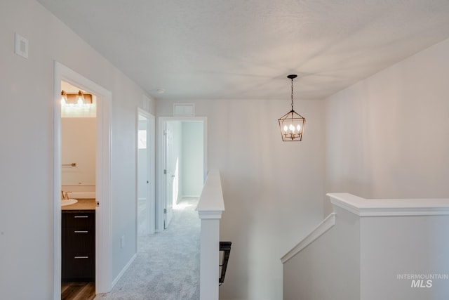 corridor featuring visible vents, baseboards, an inviting chandelier, an upstairs landing, and carpet flooring