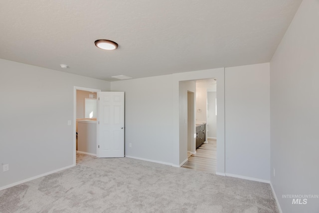 empty room featuring a textured ceiling, light colored carpet, and baseboards