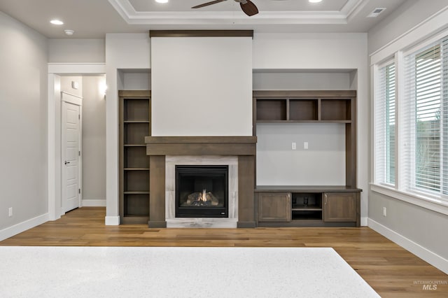 unfurnished living room with ceiling fan, a healthy amount of sunlight, light wood-type flooring, and a tray ceiling