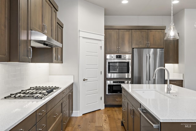 kitchen with light stone countertops, sink, stainless steel appliances, tasteful backsplash, and light hardwood / wood-style floors