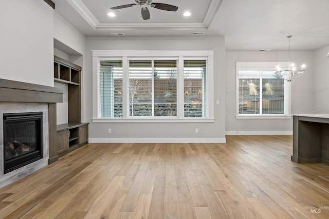 unfurnished living room featuring ceiling fan with notable chandelier, light hardwood / wood-style floors, and a raised ceiling