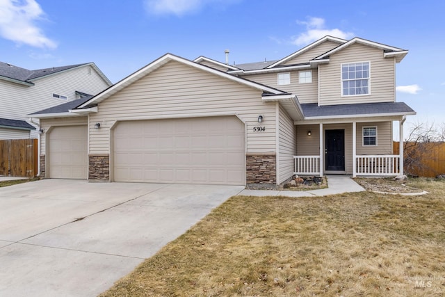 view of front facade featuring driveway, stone siding, an attached garage, fence, and a porch