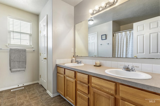 full bathroom with double vanity, a textured ceiling, visible vents, and a sink