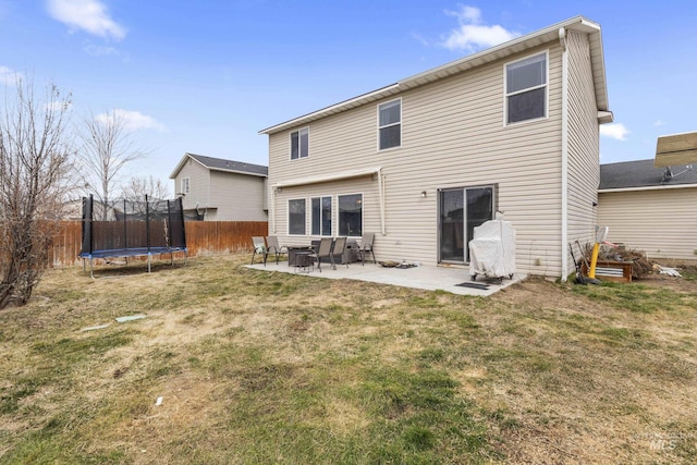 rear view of property with a trampoline, a yard, a patio, and fence