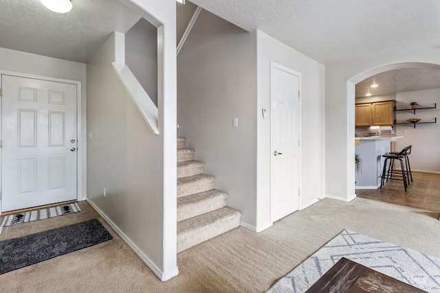 foyer entrance featuring light carpet, baseboards, arched walkways, and a textured ceiling