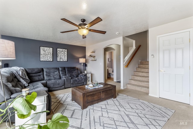 carpeted living room with arched walkways, ceiling fan, stairway, and a textured ceiling