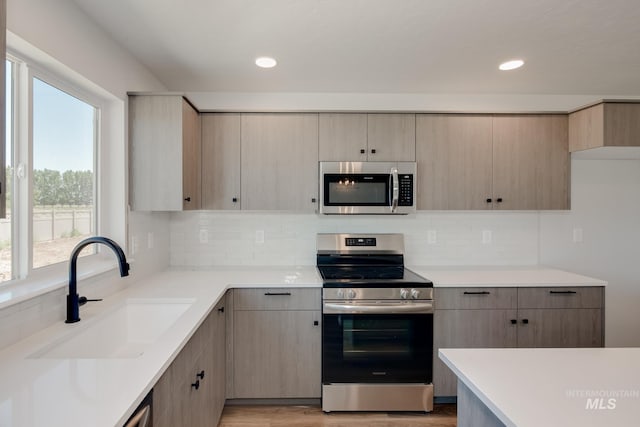 kitchen featuring stainless steel appliances, tasteful backsplash, light countertops, light brown cabinetry, and a sink