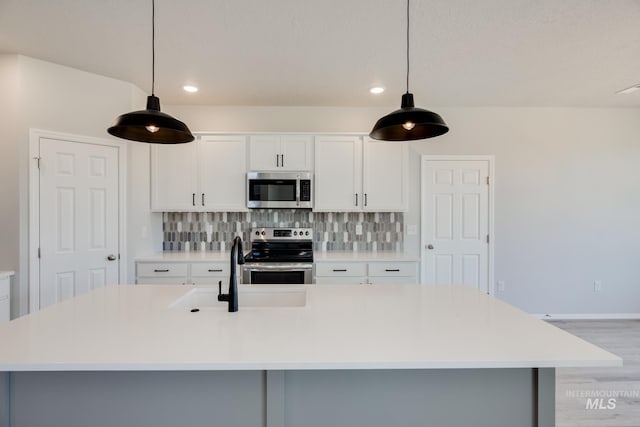 kitchen featuring light hardwood / wood-style flooring, stainless steel appliances, decorative light fixtures, and an island with sink