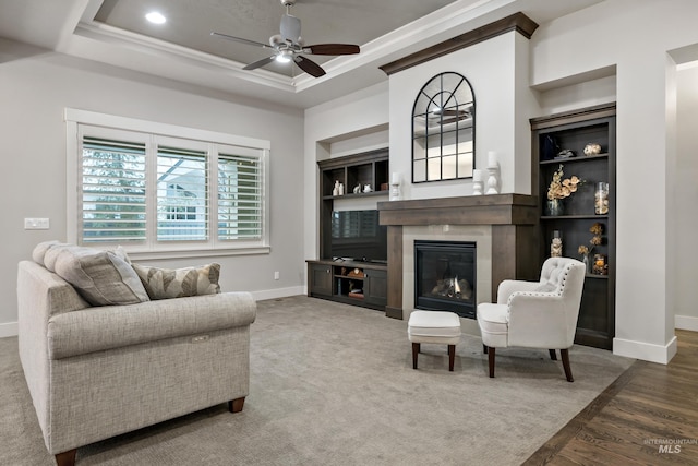 living room with ceiling fan, a raised ceiling, built in features, hardwood / wood-style flooring, and ornamental molding