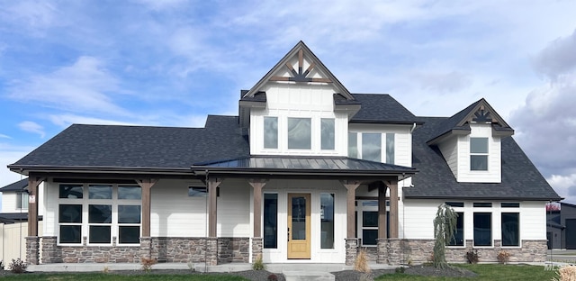 view of front of home with covered porch, a front yard, a standing seam roof, metal roof, and stone siding