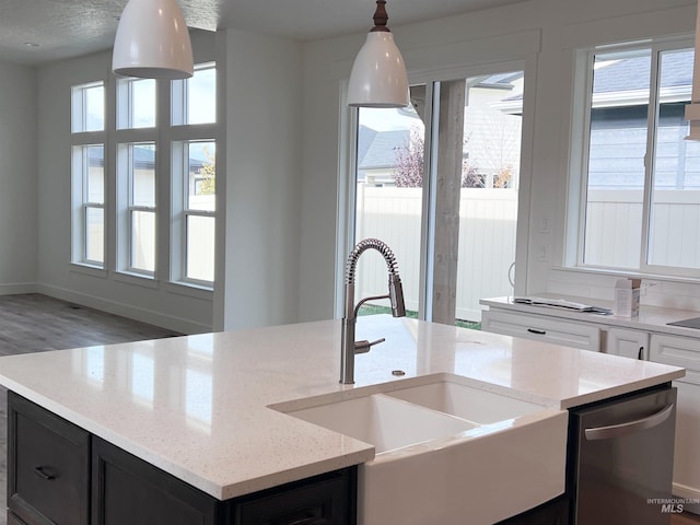 kitchen featuring light stone counters, a sink, white cabinetry, a center island with sink, and pendant lighting