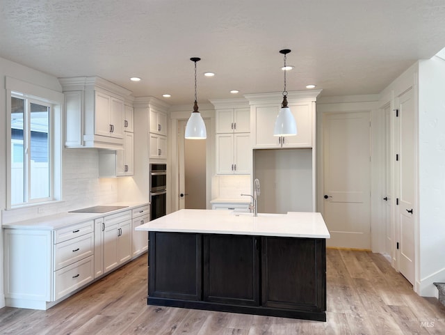 kitchen featuring pendant lighting, light countertops, black electric stovetop, and an island with sink