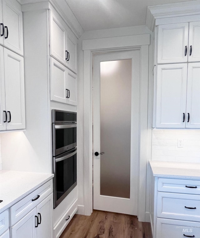 kitchen featuring tasteful backsplash, stainless steel double oven, white cabinets, and wood finished floors