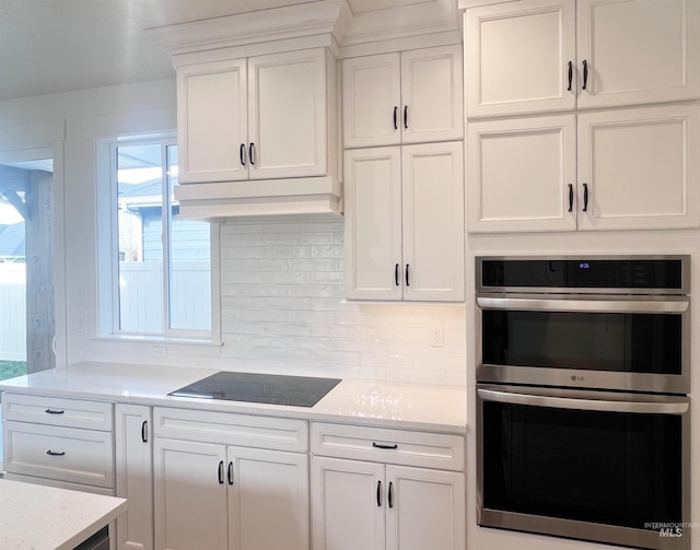 kitchen featuring double oven, black electric cooktop, white cabinets, decorative backsplash, and custom range hood