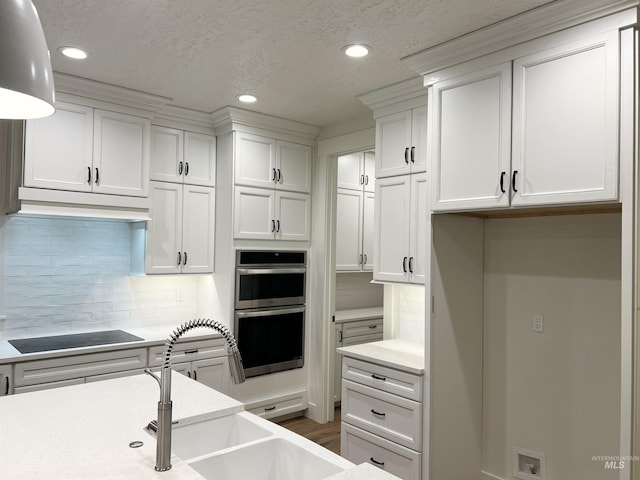 kitchen with double oven, white cabinets, light countertops, and black electric stovetop