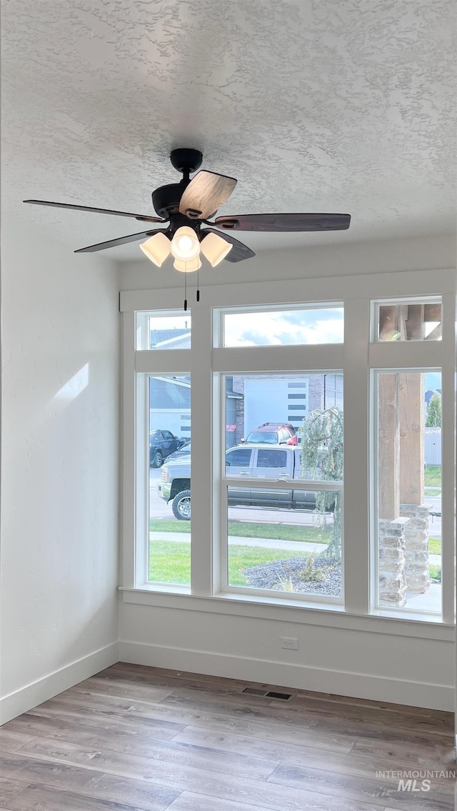 spare room with visible vents, baseboards, ceiling fan, wood finished floors, and a textured ceiling