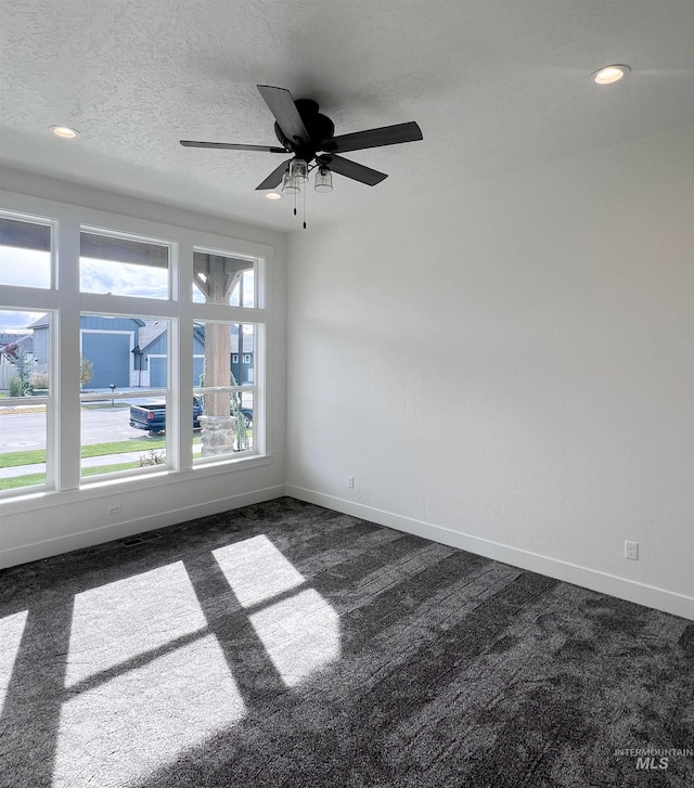 spare room with a textured ceiling, dark colored carpet, recessed lighting, and baseboards