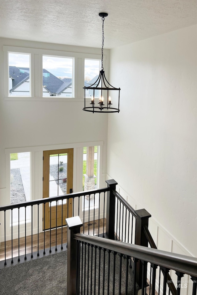 stairway featuring a wealth of natural light, a notable chandelier, a textured ceiling, and carpet