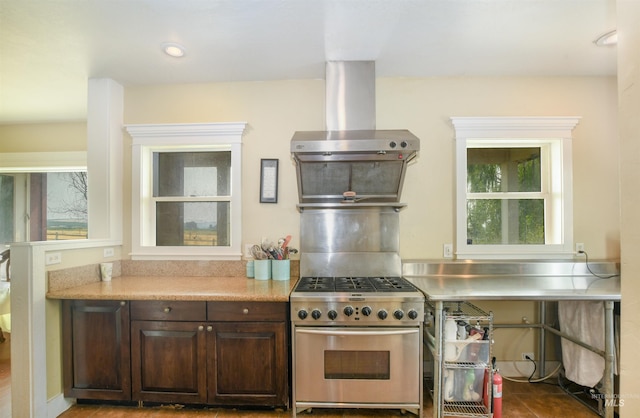 kitchen with high end stove, wall chimney exhaust hood, and dark brown cabinetry