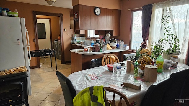 kitchen with a wood stove, white refrigerator, light tile patterned floors, washer / dryer, and kitchen peninsula