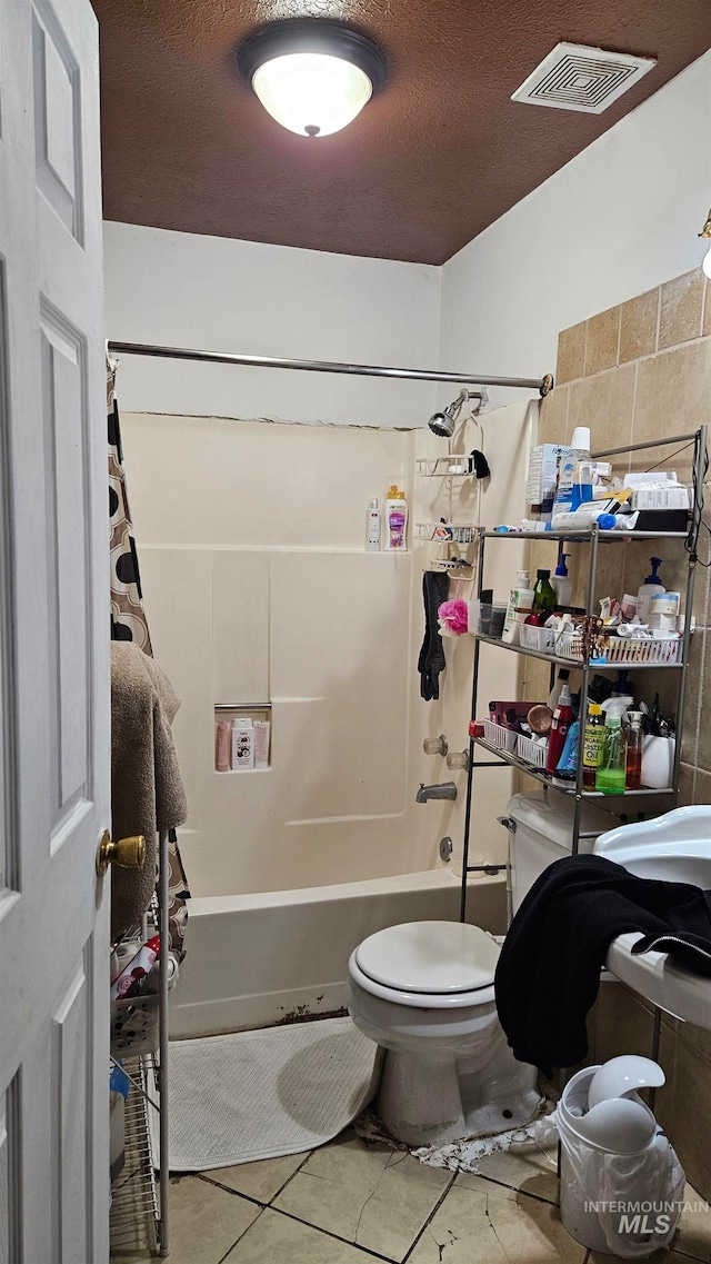 bathroom with tile patterned flooring, washtub / shower combination, a textured ceiling, and toilet