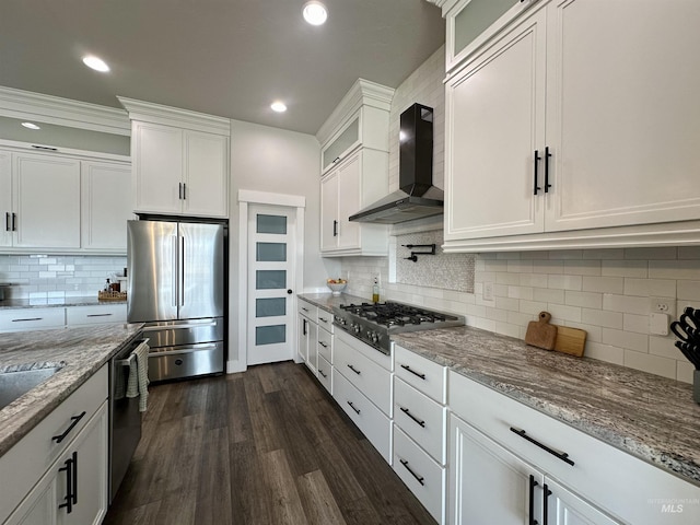 kitchen featuring light stone countertops, appliances with stainless steel finishes, wall chimney range hood, white cabinets, and dark hardwood / wood-style floors