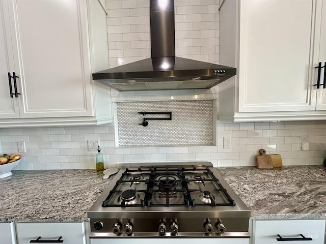 kitchen featuring white cabinetry, light stone counters, wall chimney range hood, and tasteful backsplash