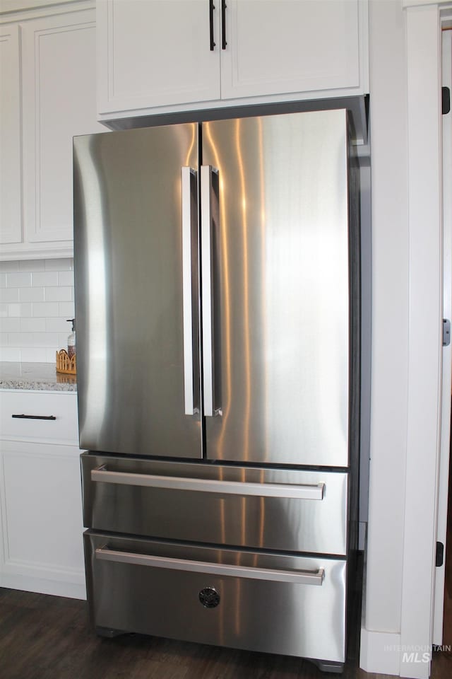 room details featuring white cabinets, stainless steel fridge, light stone counters, and backsplash