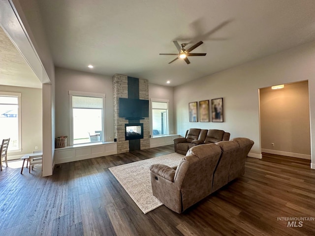 living room featuring a wealth of natural light, ceiling fan, a fireplace, and dark wood-type flooring